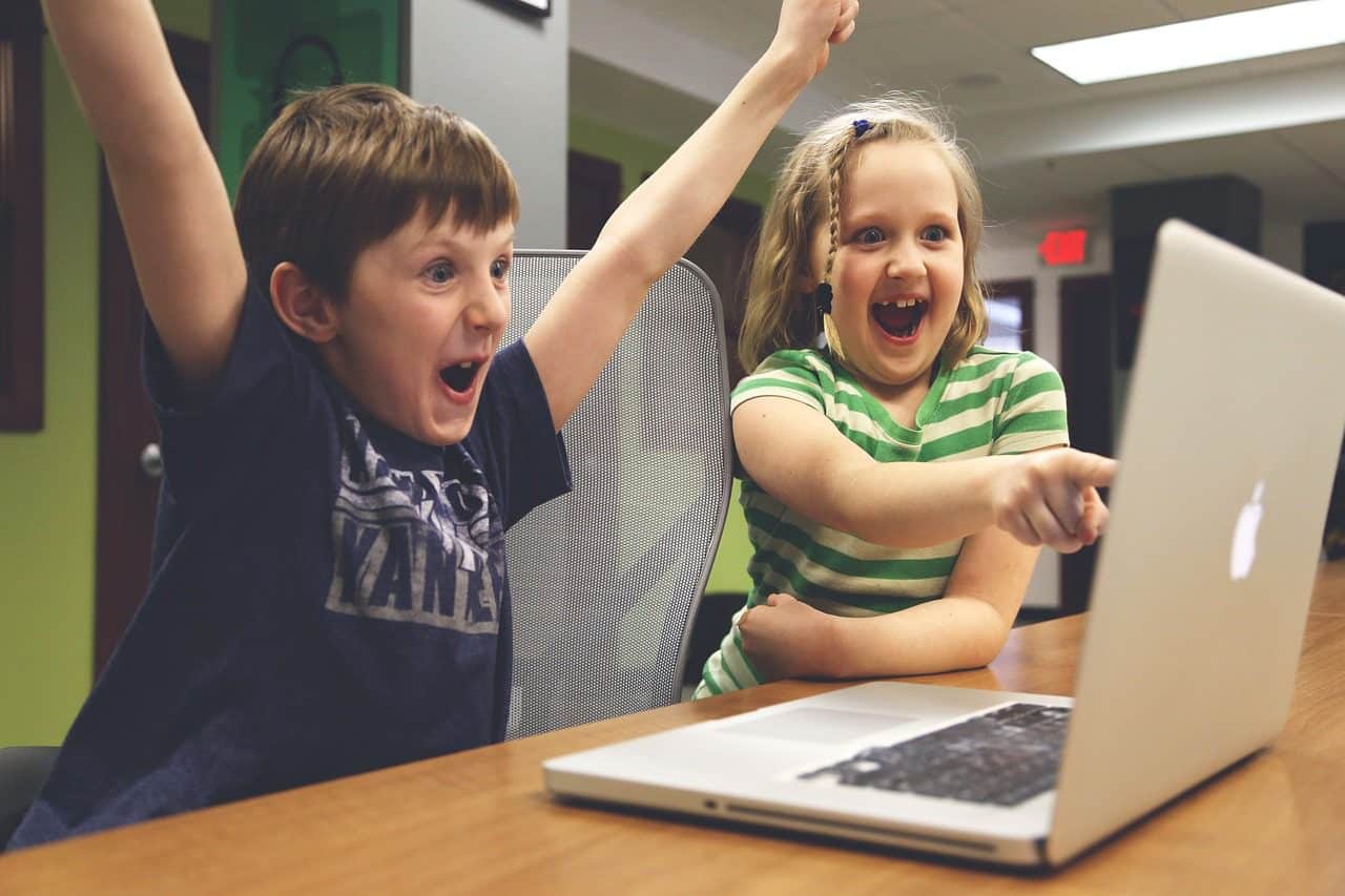 An image of a boy and a girl joyful in front of a laptop